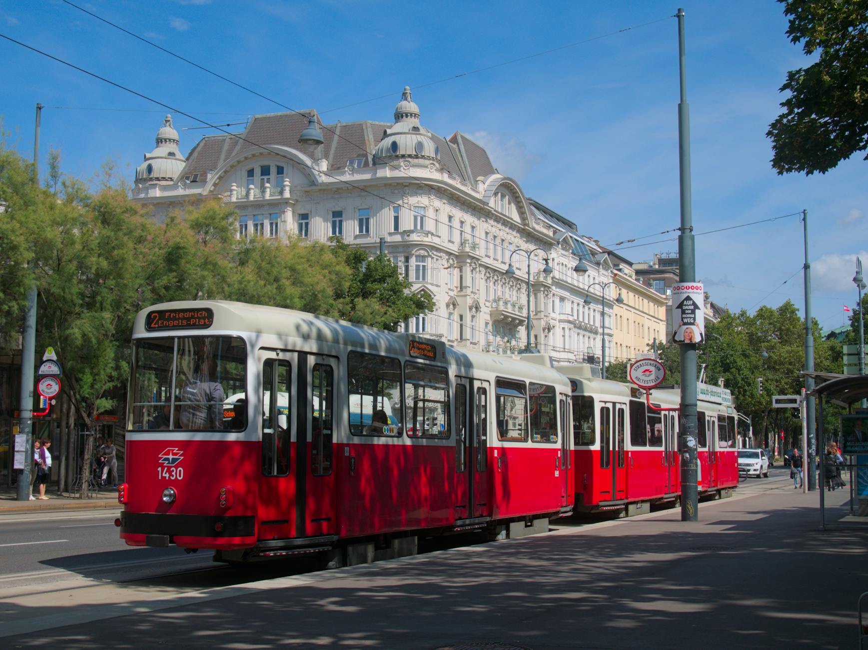 Iconic red Vienna tram traveling through scenic city streets against a bright blue sky