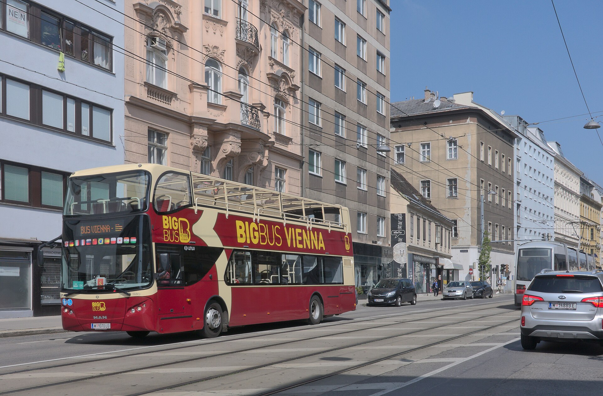 A red Big Bus Vienna open-top double-decker on a tram-lined Vienna street with a Wiener Linien tram behind it