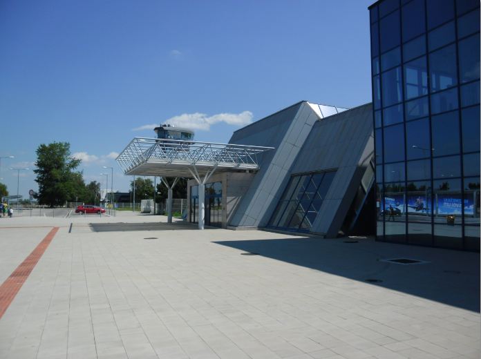 The modern steel and glass departures building at Bratislava Airport under a clear blue sky, with the control tower visible behind a canopy