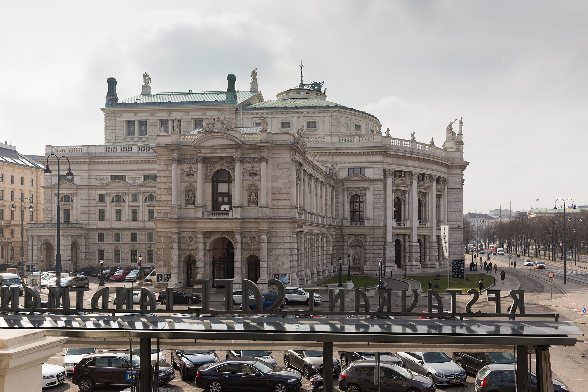 The Burgtheater in Vienna seen from an upper floor of Café Landtmann, with the reversed lettering of the café's rooftop sign in the foreground and trams on the Universitätsring to the right