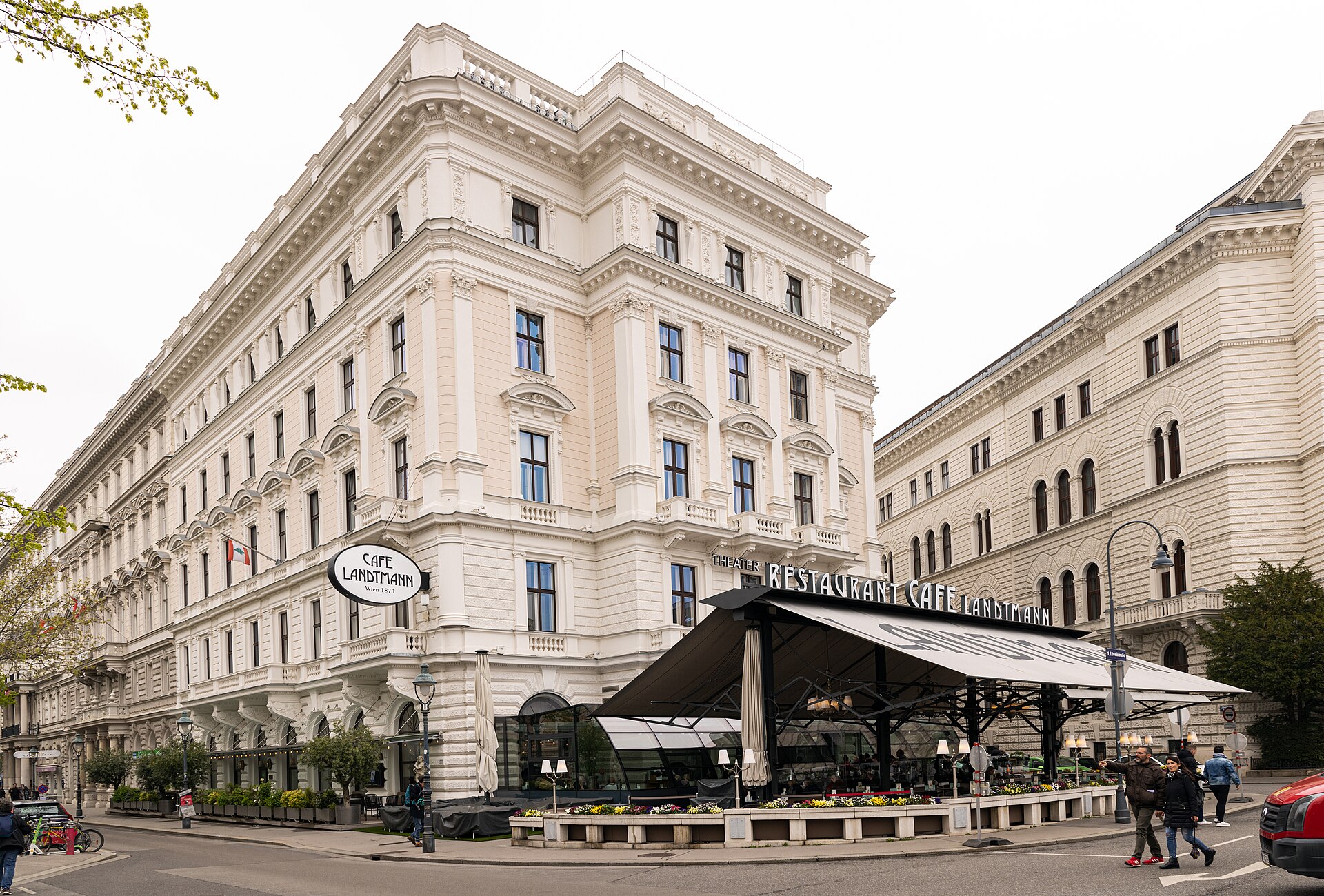 The cream-coloured corner facade of the Palais Lieben-Auspitz in Vienna, with the oval Café Landtmann sign and the café's glazed winter garden and awning-covered terrace at street level