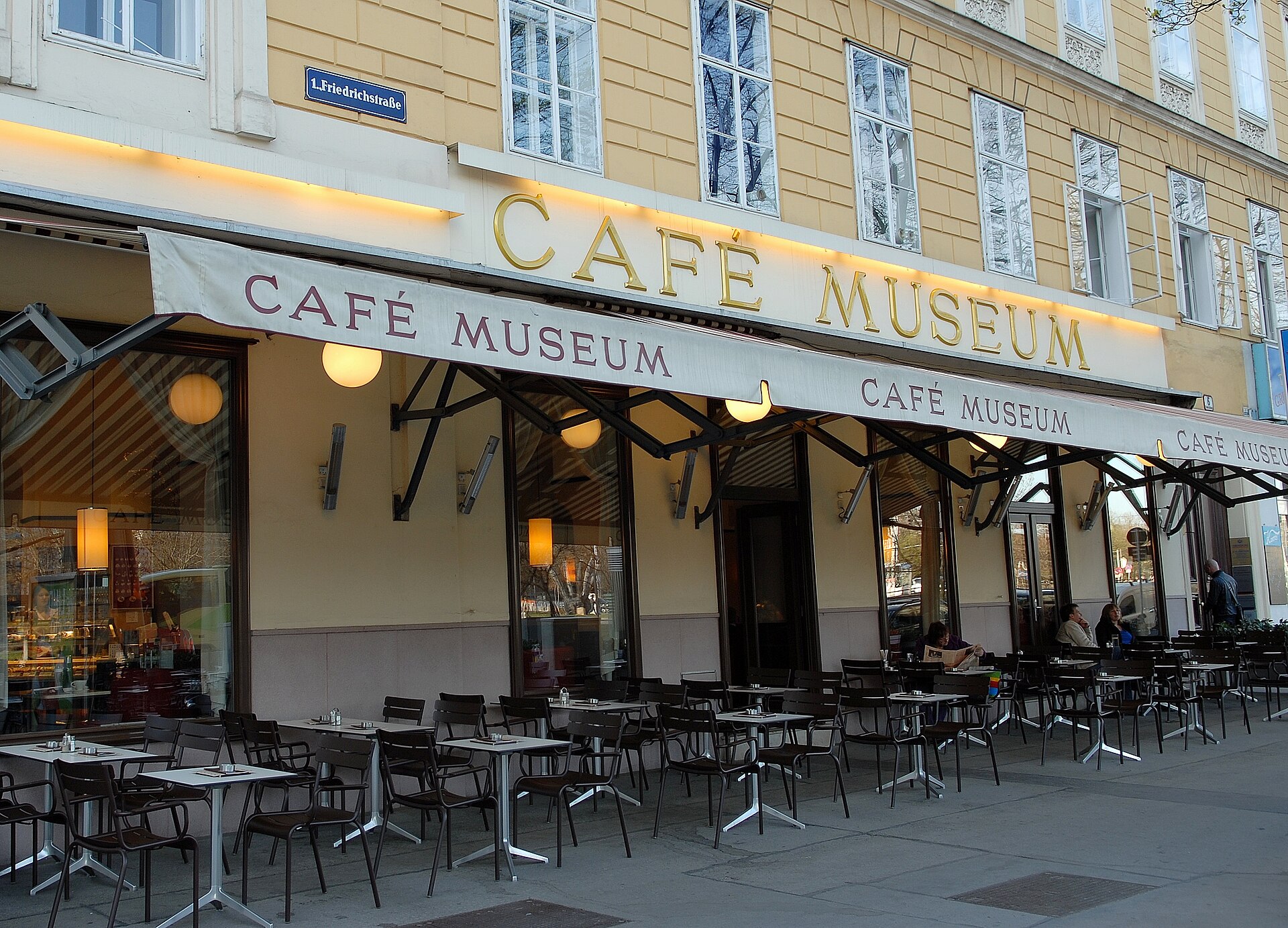 The outdoor terrace of Café Museum in Vienna, rows of empty tables and chairs beneath a cream awning with Café Museum lettering on the facade above