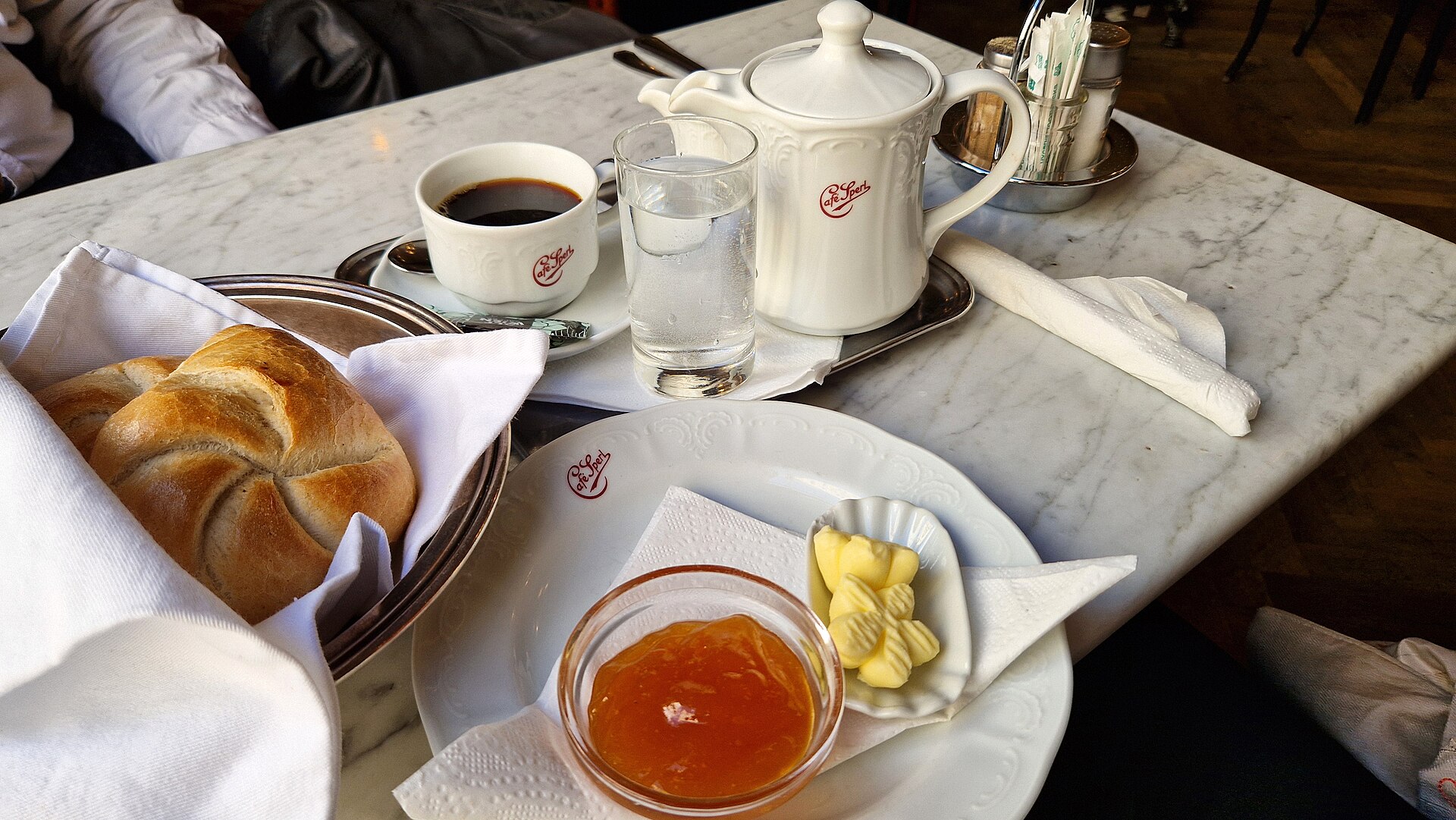 A Viennese breakfast at Café Sperl with a Kaisersemmel in a silver basket, apricot jam, butter curls and a black coffee on a marble table