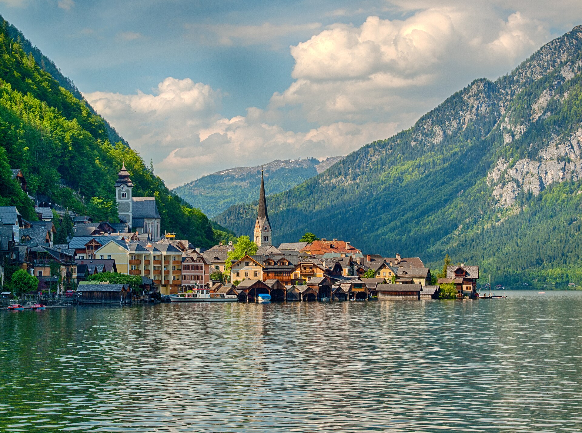 The village of Hallstatt seen across the lake, with wooden boathouses along the shore and steep forested mountains rising behind