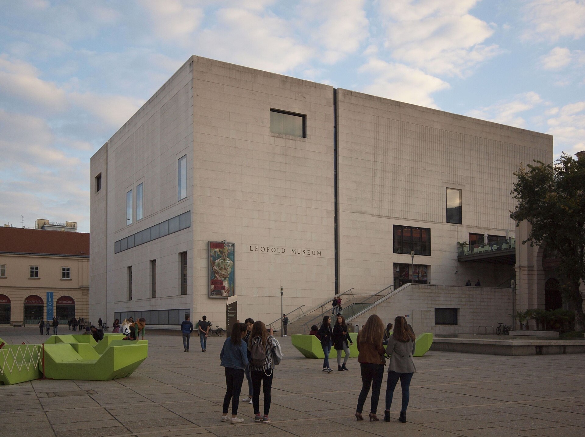 The Leopold Museum's white limestone cube in the MuseumsQuartier courtyard, with green Enzi lounge furniture and visitors on the paving in front of it