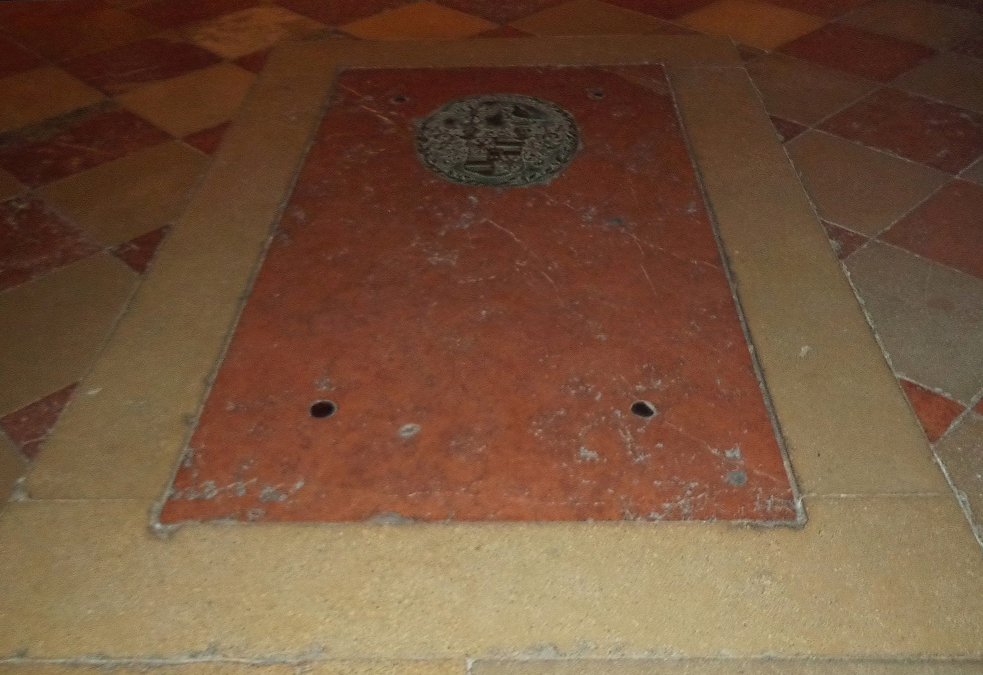 A red marble vault slab with a carved coat of arms set into the tiled floor of the Michaelerkirche