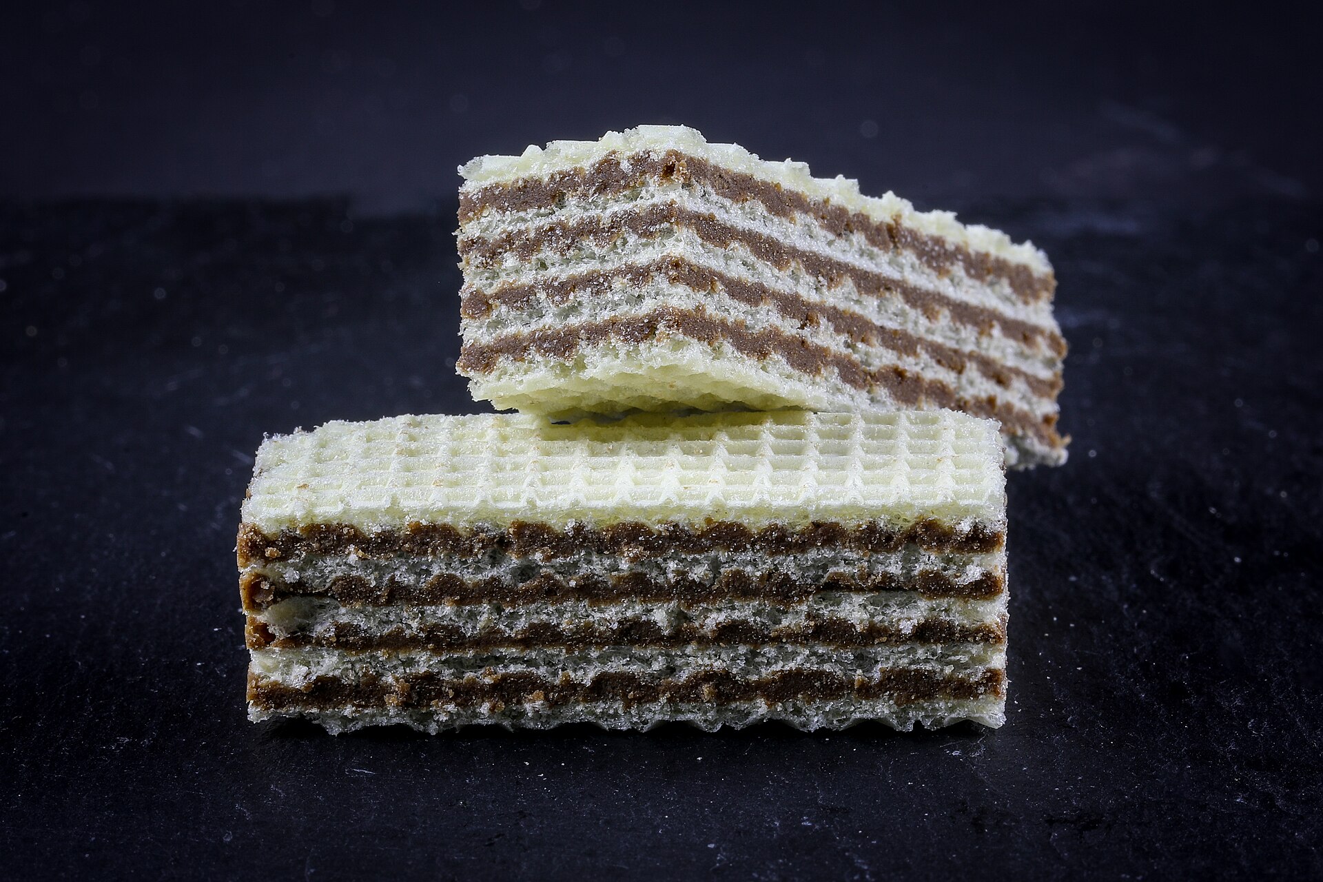 Two Neapolitan-style wafer slices with four layers of chocolate hazelnut cream photographed against a dark slate background