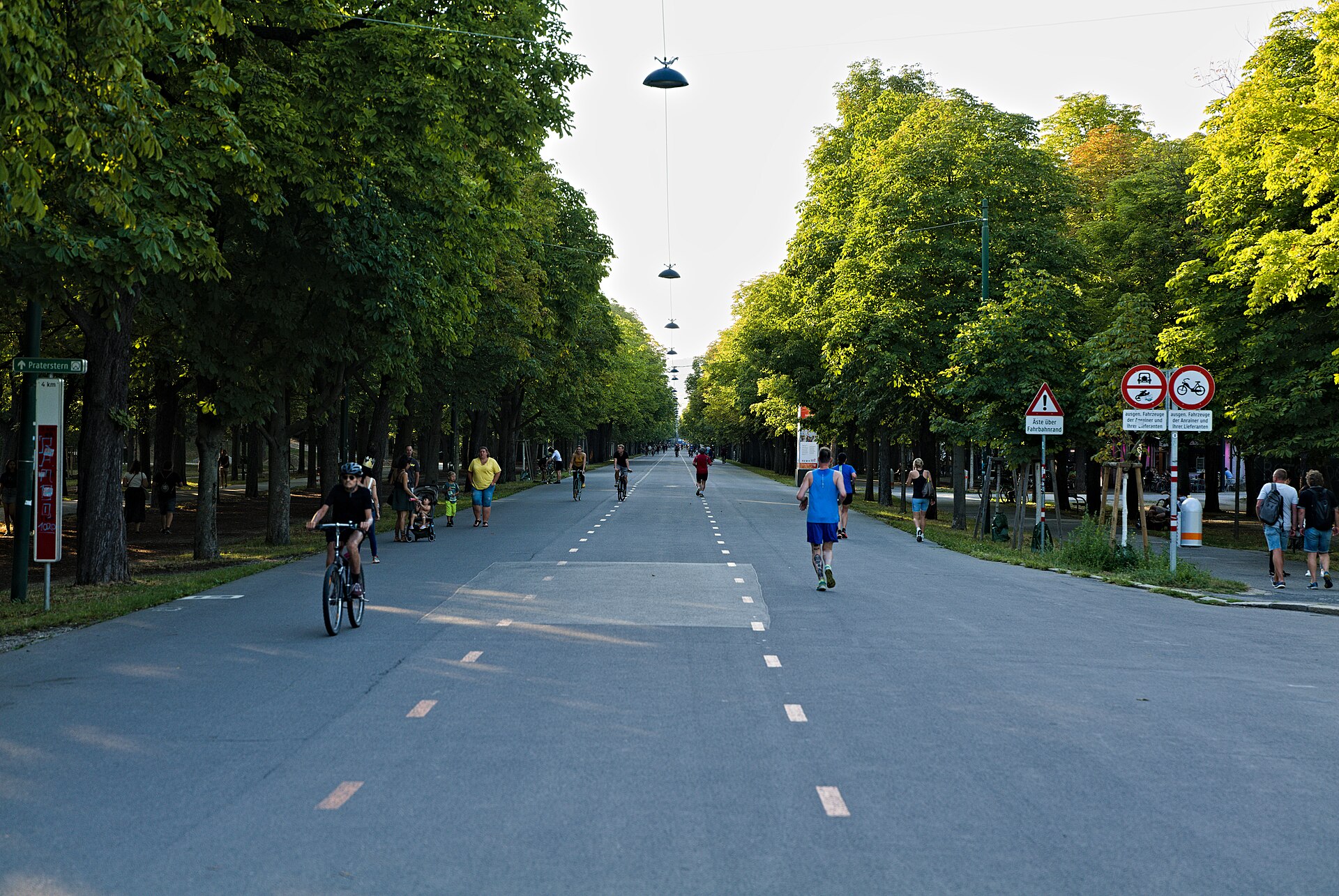 Cyclists, runners and families on the wide tree-lined Hauptallee in the Prater, with a distance marker to Praterstern