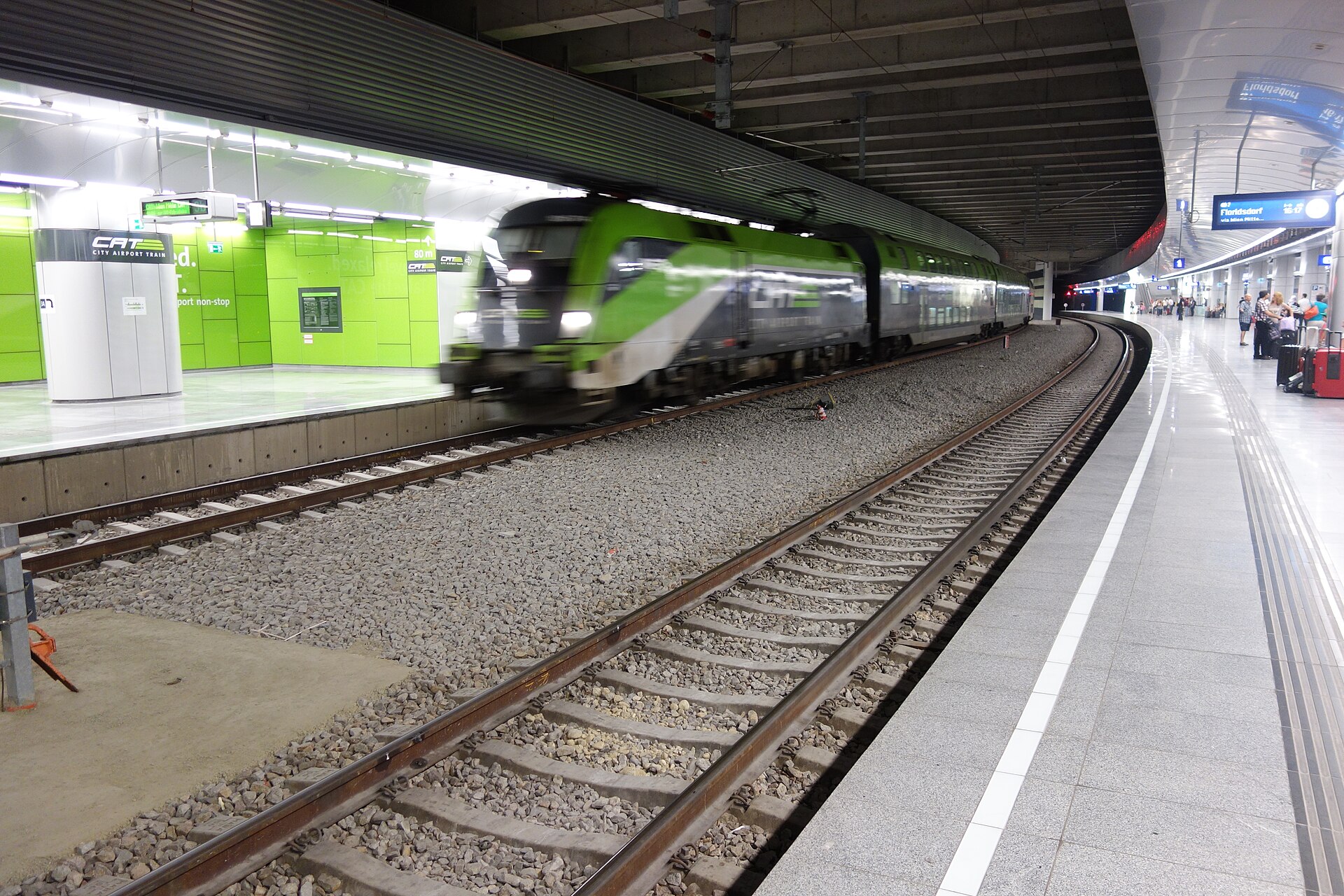 A green City Airport Train arriving at the underground railway station beneath Vienna Airport, with an S-Bahn departure board for Floridsdorf on the opposite platform