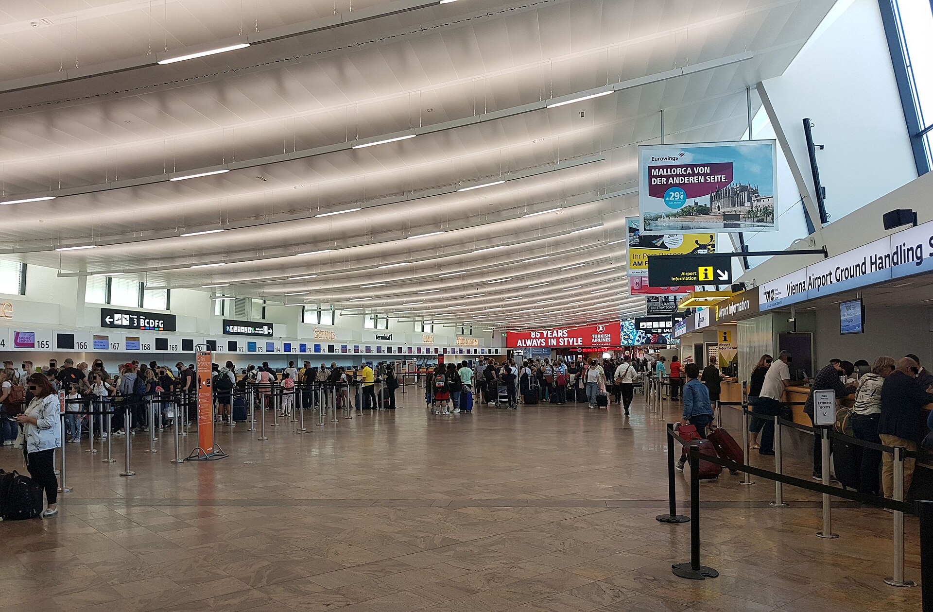 Passengers queueing at Vienna Airport check-in desks beside an airport information counter and a ground handling desk