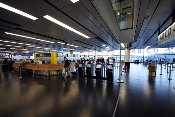 The Terminal 3 check-in hall at Vienna Airport with self-service kiosks and large A B C D gate signage above the entrance to the piers
