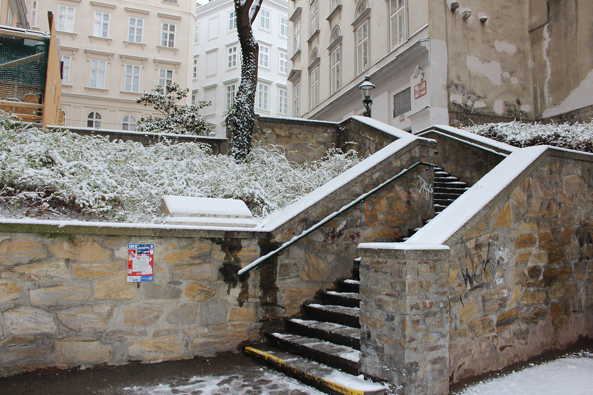 Snow-dusted stone steps and a railing beside pale Biedermeier facades in a quiet back street of Vienna's first district