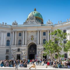 Tour groups gathered in front of the domed Michaelertor gateway of the Hofburg palace in Vienna on a clear day