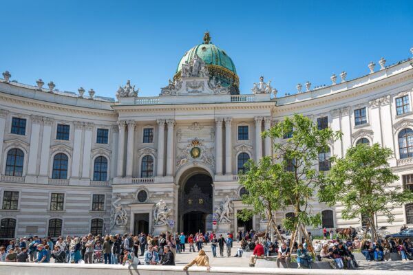 Tour groups gathered in front of the domed Michaelertor gateway of the Hofburg palace in Vienna on a clear day