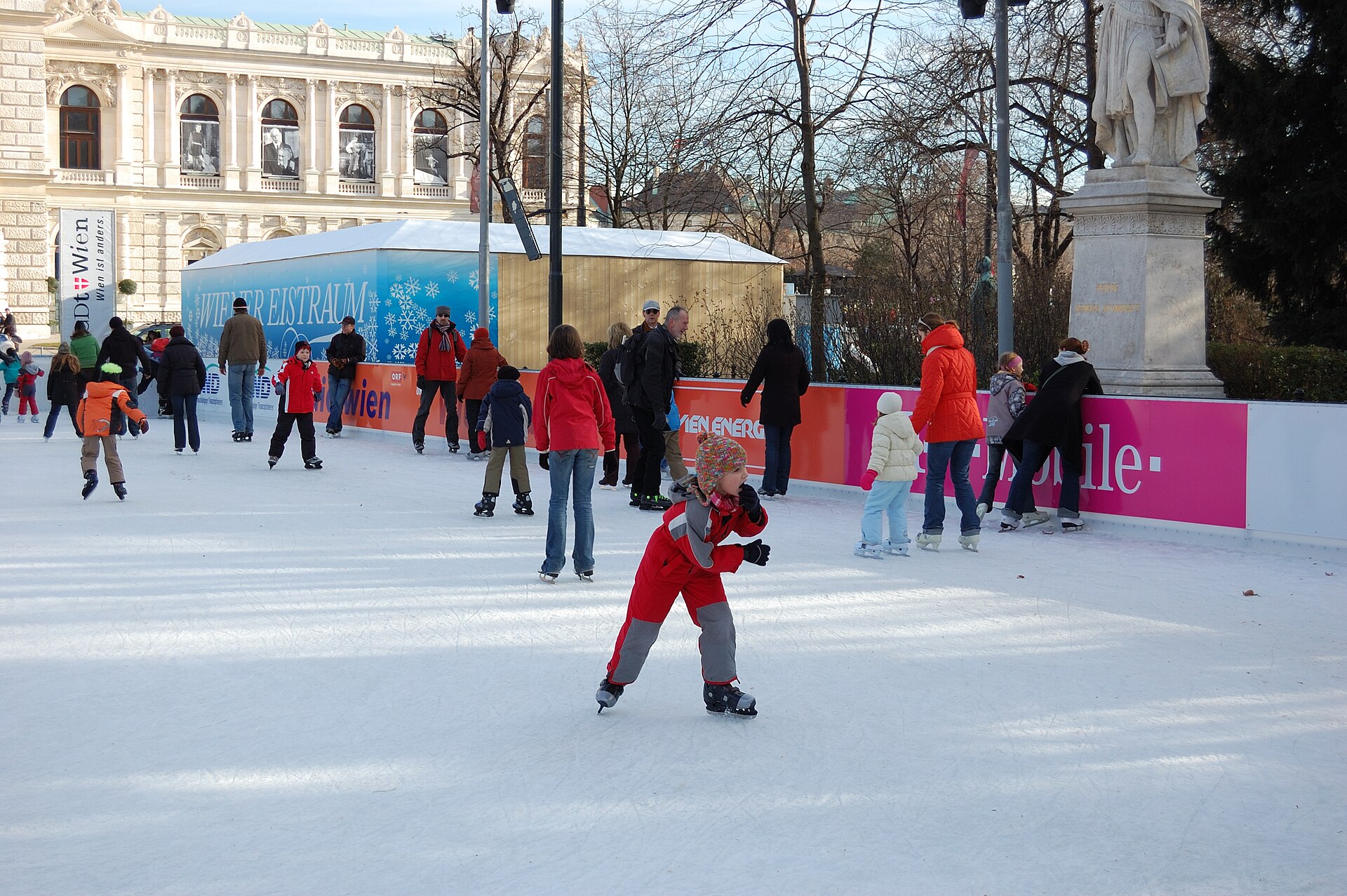 Families skating on the open-air Wiener Eistraum rink in front of the Vienna Rathaus with the Burgtheater visible behind
